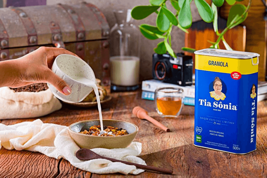 Foto com embalagem de Granola Tradicional Tia Sônia em delicioso lanche com leite e mel.